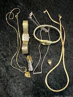 Full view of the lot on black surface showing two watches, chains, and small jewelry pieces.