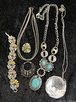 Full view of all jewelry pieces arranged on black background showing colors, shapes, and necklace chains.