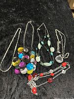 Five vintage style costume jewelry necklaces displayed on black fabric, showing details of materials and colors.