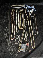 Overview of all vintage costume jewelry pieces including bead necklaces, chain necklaces with pendants, bracelets, and small accessories on a black surface.