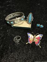 Full view of the jewelry lot containing a turquoise stone bangle watch, marquise turquoise ring, butterfly brooch, small turquoise stud earrings, and a silver open band ring.