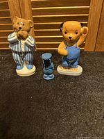 Three Wade collectible ceramic figurines displayed together against a wooden background with a pen for size reference including Baby Bear in pyjamas, Sooty, and a small blue dog figure.