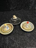 Three Wade porcelain ring dishes: two with leprechaun cobbler figurines seated on green dishes and one clear dish with a tiger figurine.