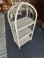 Front angle showing full 3-tier vintage wicker shelf with white painted flat shelves and floral wicker pattern sides.