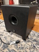 Yamaha HS8S powered subwoofer on floor with visible front port and power cord attached