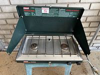 Front view of Coleman two-burner propane stove showing burners, windshields, and stainless steel cooktop surface