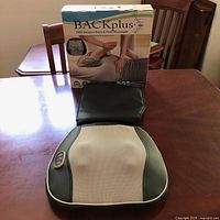 Massager unit placed on table in front of original product box showing front of the massager.