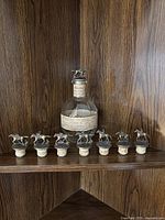 Photo showing the empty Blanton's bourbon bottle beside seven additional horse and jockey themed metal stoppers lined up on a shelf.