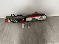 Two camping tents in their carrying bags on floor along with tent stakes and small accessories lying between them.