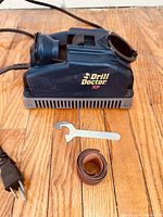 Side view of the Drill Doctor XP drill bit sharpener showing the power cord, metal wrench, and sanding belt.