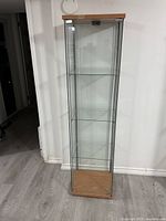 Full view of glass display case showing wood top and base with glass sides and door