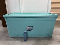 Full front view of a large blue/teal Sterilite storage bin with lid, showing size comparison to a water bottle placed in front.
