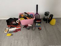 Photo showing the full lot including tool bag, pink bin with cords, bug zapper racket, two lanterns, and camping accessories on floor.