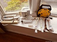 Photo of multiple electrical cords, power strips and adapters arranged on windowsill