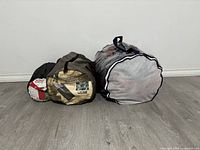 Three sleeping bags compressed inside their storage sacks on a gray floor against white wall, showing size differences and bag colors.