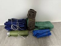 Overall view of five tarps in various colors folded, rolled, and tied, showing different sizes and storage methods.