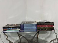Photo showing three stacks of auction catalogues on a glass table, mostly Sotheby's catalogues in blue covers with some black, red, and white-covered catalogues tied with rubber bands.