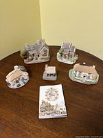 Top view of four vintage miniature English cottages and a color illustrated booklet on a round wooden table.