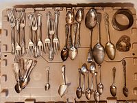 Assorted flatware laid out including multiple forks, spoons, serving pieces and napkin rings