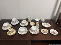 Full lot of assorted vintage teacups, saucers, creamers, sugar bowls and plates displayed on a table, showing different styles and colors