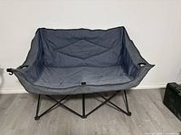 Unfolded loveseat camping chair showing the fabric seat and backrest, metal frame, and cup holders on each side.