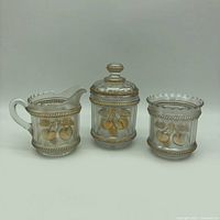 Front view of the three-piece white carnival glass set with gold peach and cable design.