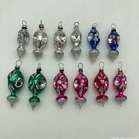 Full lot of 12 vintage mercury glass Christmas ornaments in various colors laid out flat showing shape, glitter decoration, and hanging loops.