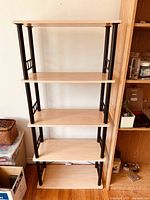 Full frontal view of five-tier shelving unit, showing light wood shelves supported by black metal columns and decorative side rails.