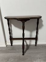 Front view of the vintage demi lune wooden table showing its shape, turned legs, and wear.