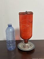 Front view of vintage red hummingbird feeder next to a plastic water bottle for size comparison.