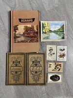 Photo showing vintage scrapbook, two 1930s journals, painting, and vintage postcards arranged on a surface