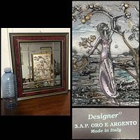 Full view of the framed wall art with water bottle for scale, showing the dark red woodgrain frame surrounding the mirrored frame featuring the silver bas relief at center.