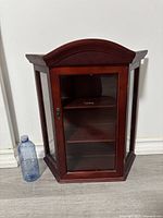 Front view of the wooden curio display shelf showing glass door, arched top, and side glass panels.