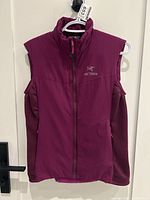 Front view of women's Arc'Teryx vest in raspberry color, hanging on a hanger showing logo and zipper details.