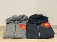 Two folded hoodies front view, dark grey and light grey, showing front chest heart and lightning bolt motif