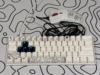 Glorious Model O gaming mouse placed on the keyboard, showing mouse cable and keyboard with custom blue WASD keys and patterned spacebar with black contour pattern on white keys.