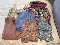 Seven pieces of girls clothing laid out including puffer jacket, dresses, skirts, cardigans and lounge sets