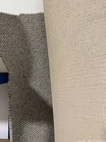 Close-up photo showing the edge of the grey wool carpet with its looped texture and woven beige backing material.