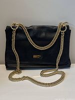 Front view of black leather flap bag with gold-tone chain strap draped over
