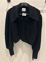 Front view of black knit cropped sweater showing wide collar, textured knit pattern and sleeve fringe detail