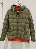 Front view of olive green Holden down filled jacket with hood and orange lining, hanging on a hanger.