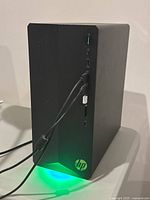 Three-quarter front view showing textured front panel, HP logo, green LED lighting and connected cables