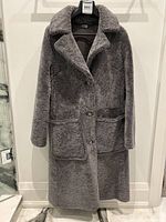 Front view of full-length grey reversible shearling coat hung on hanger