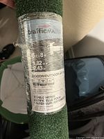 Close-up photo of the label on the artificial turf roll showing dimensions 6x8 ft, brand TrafficMASTER, indoor/outdoor use, material info
