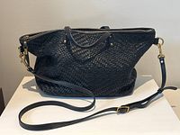 Front view of black woven leather bag with detachable strap laid on white surface