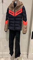 Front view of Fire + Ice jacket and black ski pants on hanger