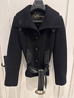 Front view of the Mackage black textured wool jacket with button closure, wide collar, leather trim on pockets and belt detail.