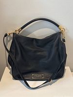 Front view of bag showing pebbled leather exterior, top handle, adjustable strap and Marc Jacobs nameplate