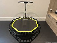 Front-facing view of octagonal exercise trampoline with adjustable handlebar, showing One Two Fit logo and yellow trim around mat edge.