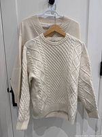 Front view of cable knit and V-neck sweaters on hangers